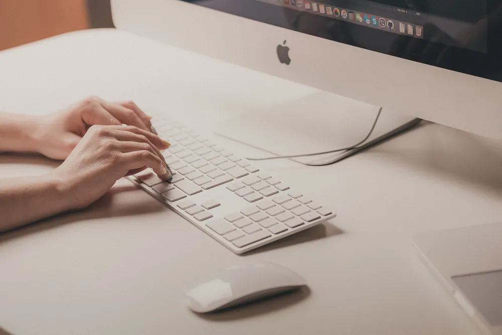 صورة ليدَي امرأة على لوحة مفاتيح جهاز Mac، تستعدان لكتابة عرض أعمال