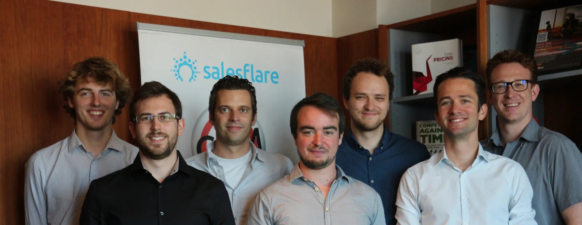 فريق Salesflare المؤلف من سبعة أشخاص مصطفًّا في المكتب أمام لافتة Salesflare
