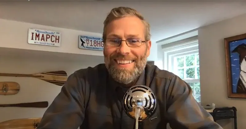 Dave Will of PropFuel smiling behind a podcast microphone at home, canoe paddles and Massachusetts licence plates on the wall