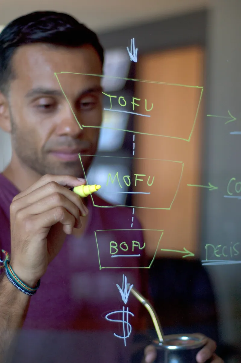 A man drawing a funnel on a glass wall, its three stages labelled TOFU, MOFU and BOFU, with a dollar sign below