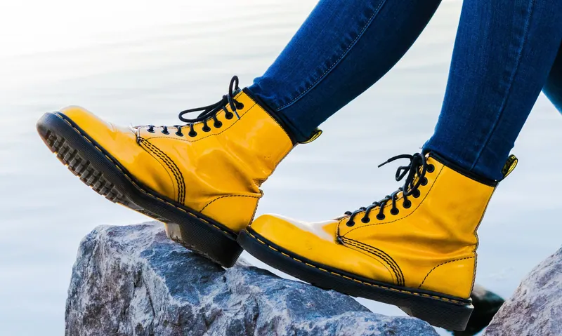Des bottes jaunes à lacets, style Dr. Martens, franchissant un rocher au bord de l'eau